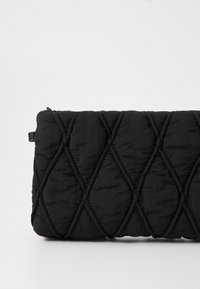 Černá prošívaná kabelka ve tvaru obálky s diamantovým vzorem a hladkou strukturou. Zapínání na zip a malá rukojeť na jedné straně.