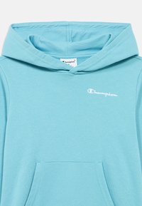 Φωτεινά γαλάζια φούτερ με κουκούλα, με μπροστινή τσέπη, απαλή υφή και μικρό λευκό λογότυπο Champion στο στήθος. Σχεδιασμένο με κουκούλα που δένεται με κορδόνι.