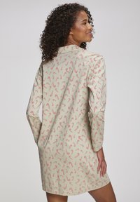 Beige kjole med et gjentakende mønster av røde sukkerrør, lange ermer og krage, med en avslappet passform og glatt tekstur.