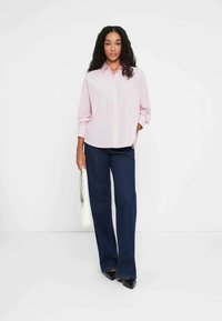 Camisa de mangas longas rosa clara com frente de botões, combinada com jeans de perna larga azul escura. Os acessórios incluem uma bolsa branca e sapatos pretos.