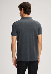 Graues kurzärmliges Poloshirt mit klassischem Kragen, aus Strickstoff hergestellt. Verfügt über ein Etikett an der Seite. Glatte Textur mit maßgeschneidertem Schnitt.