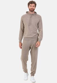 Ensemble sweat à capuche beige et pantalon de jogging en matière douce, avec capuche à cordon de serrage et taille élastique, assorti à des baskets blanches.