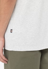 Ljusgrå kortärmad t-shirt i bomull med en slät yta. Har en liten logotagg på nederkanten. Matchas med olivgröna byxor.