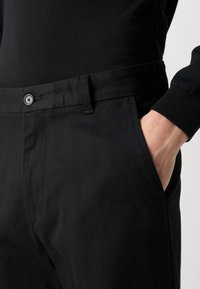 Black trousers feature a straight cut with a smooth texture, a front pocket, and a matching belt. The fabric appears lightweight and durable.