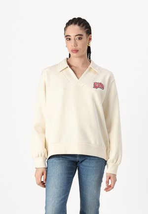 Sweatshirt bej cu guler în V, manșete ribbed și logo-ul „1990” brodat în roșu. Material moale, cu o croială lejeră.