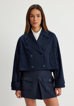 Marineblauwe cropped dubbelbreasted jas met grote revers, knoopaccenten en voorzakken, gecombineerd met bijpassende shorts met zijzakken.
