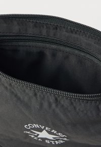 Μαύρο υφασμάτινο θήκη με φερμουάρ, με λευκό λογότυπο "Converse" και σχέδιο αστεριού, εσωτερικό χωρίς επένδυση και ευρύχωρο.