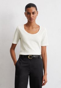 Witte T-shirt met korte mouwen en een ronde hals, gecombineerd met zwarte broek en een zwarte riem met een gouden gesp. Gladde, gestructureerde stof.