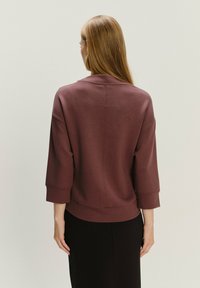 Sudadera burdeos con mangas tres cuartos, tejido texturizado y un corte relajado. Presenta un escote redondeado y detalles de costura sutiles.