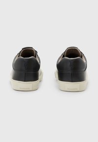 Schwarze Leder-Sneaker mit glatter Oberfläche, kontrastierender kremfarbener Sohle, geprägtem Logo an der Ferse und schnittigem Low-Top-Design.