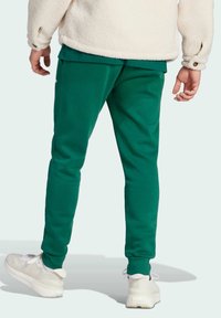 Green sweatpants made of soft fabric, featuring a tapered leg design and elastic cuffs, paired with white sneakers on a light background.