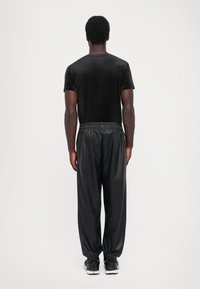 Camisa preta de veludo com mangas curtas e colarinho bordeaux, combinada com calças pretas, brilhantes e de corte largo, com cintura elástica.