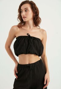Top nero senza spalline con un design arricciato e texturizzato. Presenta un elastico e un dettaglio con cordoncino. Il tessuto è leggero e stropicciato.