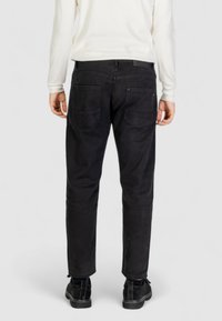 Pantaloni neri in cotone con vestibilità dritta, dotati di due tasche posteriori e un design pulito, abbinati a scarpe in suede nere.