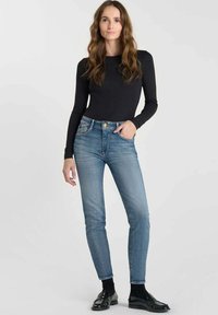 Jean skinny bleu avec des zones décolorées, taille haute et cinq poches. Associé à un haut noir à manches longues et des chaussures noires.
