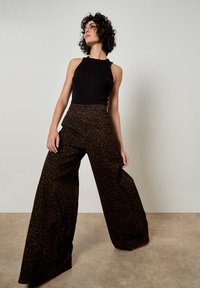 Leopardenmusterweite Hosen mit hoher Taille und strukturiertem Stoff, kombiniert mit einem enganliegenden schwarzen ärmellosen Oberteil. Glatte Oberflächenbeschaffenheit.