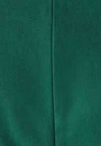 Žalia medžiaga su lygiu paviršiumi ir subtiliu blizgesiu. Paviršiuje matyti austo rašto detalės, kuriose yra raukšlė arba siūlė.