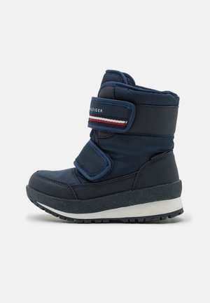 Mørkeblå isoleret vinterstøvle med to velcroremme, tyk sål med mønster og detaljeret rem med mærke på ensfarvet baggrund.