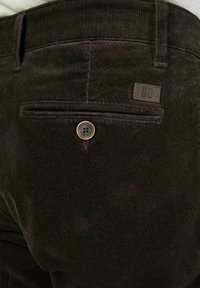 Braune Cordhosen mit einer Gesäßtasche mit Knopfverschluss und einem kleinen Markenlogo-Tag über der Tasche. Weicher, strukturierter Stoff.