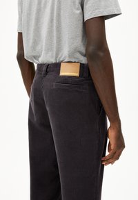 Donker corduroy broek met een gestructureerd oppervlak, tailleband met riemlussen, en een bruine leren label met "ARMEDANGELS."