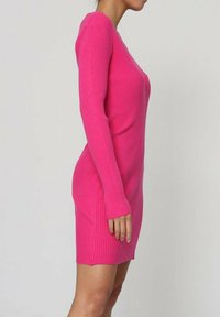 Robe rose à côtes avec des manches longues, silhouette ajustée et Ourlet au genou. La texture est lisse avec un détail à côtes verticales.