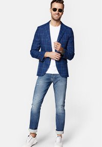 Niebieski marynarka w kratkę z klapami, założona na białą koszulkę, w zestawie z podartymi jasnoniebieskimi dżinsami i białymi trampkami. Brązowe okulary przeciwsłoneczne.