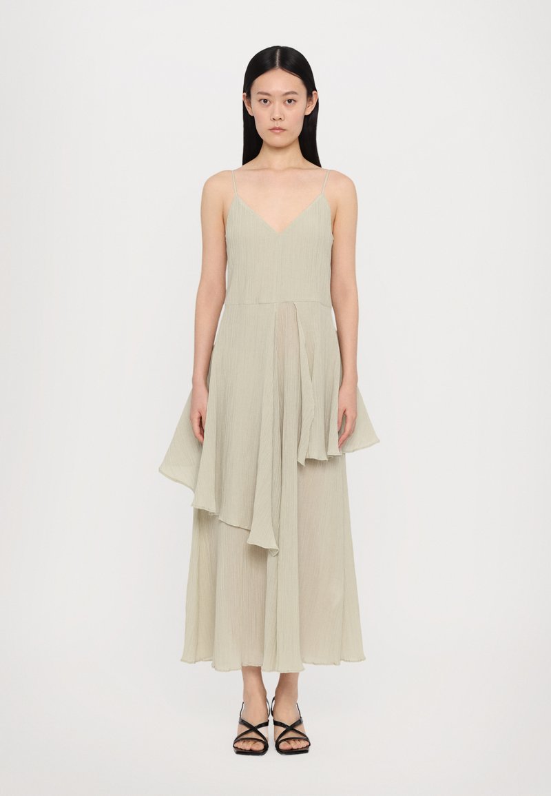 Light green, sleeveless dress with a deep V-neck, flowing, layered skirt, and textured fabric. Paired with black strappy sandals.