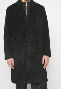 Sort, tekstureret, oversized frakke lavet af blødt materiale, med en krave med spidser og to frontknapper, lange ærmer og en afslappet pasform.