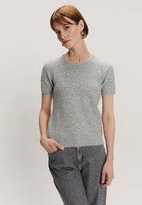 Grijze kortste mouw sweater van zachte gebreide stof, met een ronde halslijn en subtiele textuur, gecombineerd met grijze jeans.