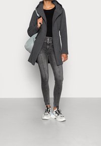 Abrigo gris con capucha sobre un top negro acanalado, combinado con jeans ajustados grises y zapatillas blancas con detalles en azul claro. Bolso azul claro colgado del hombro.