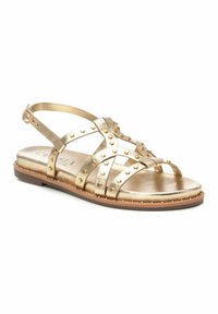 Sandal metallic dorado que presenta múltiples tiras con tachuelas, una tira en el tobillo con hebilla y una suela plana con un suave borde marrón.