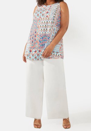Top sans manches à motifs floraux multicolores, avec une coupe décontractée. Assorti à un pantalon blanc ample et des sandales métalliques à lanières.