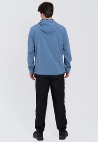 Chaqueta azul, ligera, con capucha y puños elásticos, combinada con pantalones cargo negros que presentan múltiples bolsillos y una tela texturizada.