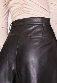 Svart läderbyxor med slät textur, som har två bakfickor och en skräddarsydd passform vid midjan. Försedda med en bältesögla.