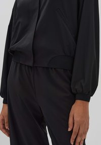 Schwarze sportliche Jacke mit einem cropped Design, weicher Textur, großen Ballonärmeln und seitlichen Taschen. Verfügt über gerippte Bündchen und Saum.