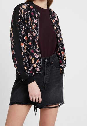 Persoon die een zwarte bloemenritsvest draagt, een donker bordeauxrood topje en een zwarte high-waisted denim rok met rafelige zoom.