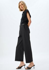 Top nero senza maniche con spalle strutturate, abbinato a pantaloni neri a vita alta e sandali con tacco trasparente; tessuto liscio e vestibilità sartoriale.