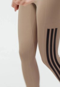 Beige athletic leggings featuring a sleek design, made from stretchy material, with three vertical black stripes on the side.