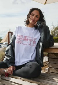 Witte T-shirt met korte mouwen met daarop de rode grafische tekst "GIRL DINNER" en illustraties van noedels, een martini, kaas en chocolade.