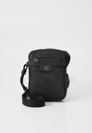 Sac bandoulière noir compact avec poche avant zippée et sangle ajustable, avec logo HUGO embossé sur le rabat avant.
