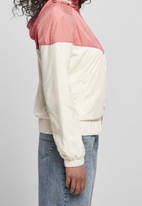 Lekka kurtka w różowo-kremowym wzorze color block, z kapturem, ściągaczami na mankietach, elastycznym pasem i bocznymi kieszeniami.