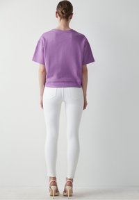 Lila bomullströja med korta ärmar, i kombination med vita leggings och nakna klackar. Tyget ser mjukt och avslappnat ut.