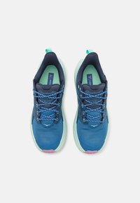 Sinivihreät ja turkoosit urheilukengät, joissa on teksturoitu verkkomateriaali päällisessä, kontrastiväriset nauhat ja vaaleanpunaisin yksityiskohdin varustettu pehmustettu pohja.