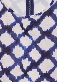 Mönstrad textil med en blå och vit design med en diamantform i olika nyanser av blått. Mjuk, lätt tygtextur.