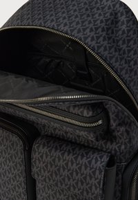 Μαύρο και γκρι σακίδιο με σχέδιο, πολλαπλές θήκες με φερμουάρ, δύο μπροστινές τσέπες και επένδυση εσωτερικού με λογότυπο.