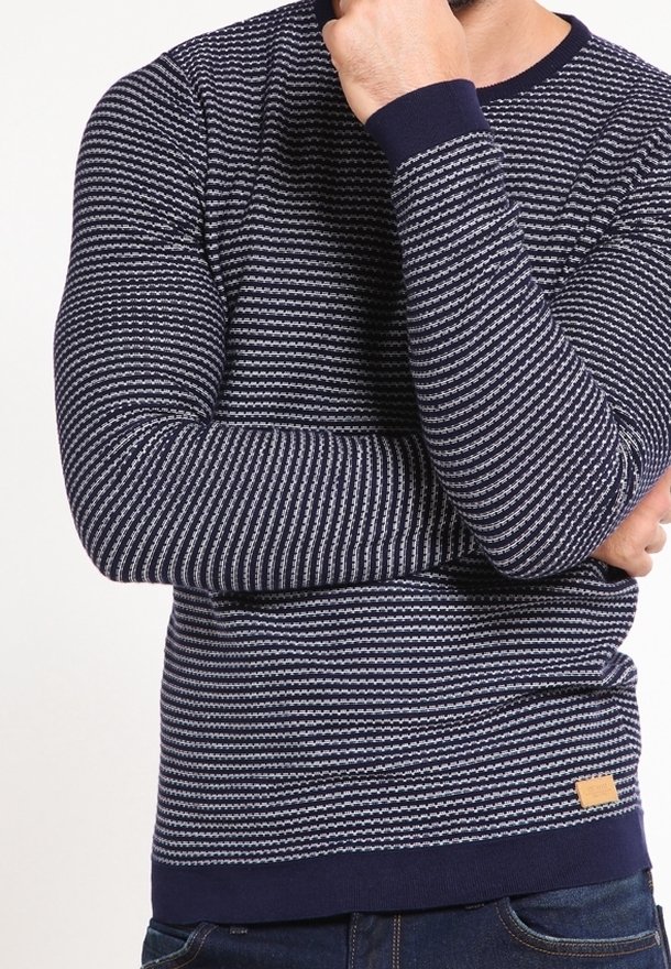 Laivastonsininen pitkähihainen villapaita valkoisilla vaakaraitoja, pyöreä kaula-aukko, resorit hihansuissa ja pieni ruskea nahkalappu helmassa.