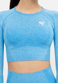 Blå långärmad croppad topp med ett strukturerat mönster, ribbat avslut och en liten vit logotyp på bröstet. Slätt, elastiskt tyg.