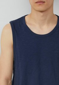 Navy blue sleeveless tank top, made of lightweight cotton blend fabric, featuring a round neckline and subtle texture. Small logo on the chest.