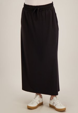 Zwarte rok tot net boven de enkel met elastische tailleband en trekkoord, gedragen met witte sneakers met beige strepen en rubberen zolen.