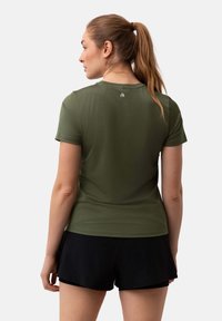 Olivgrünes, kurzärmliges Sportshirt mit texturierter Oberfläche und kleinem Logo auf dem Rücken, kombiniert mit schwarzen Shorts.